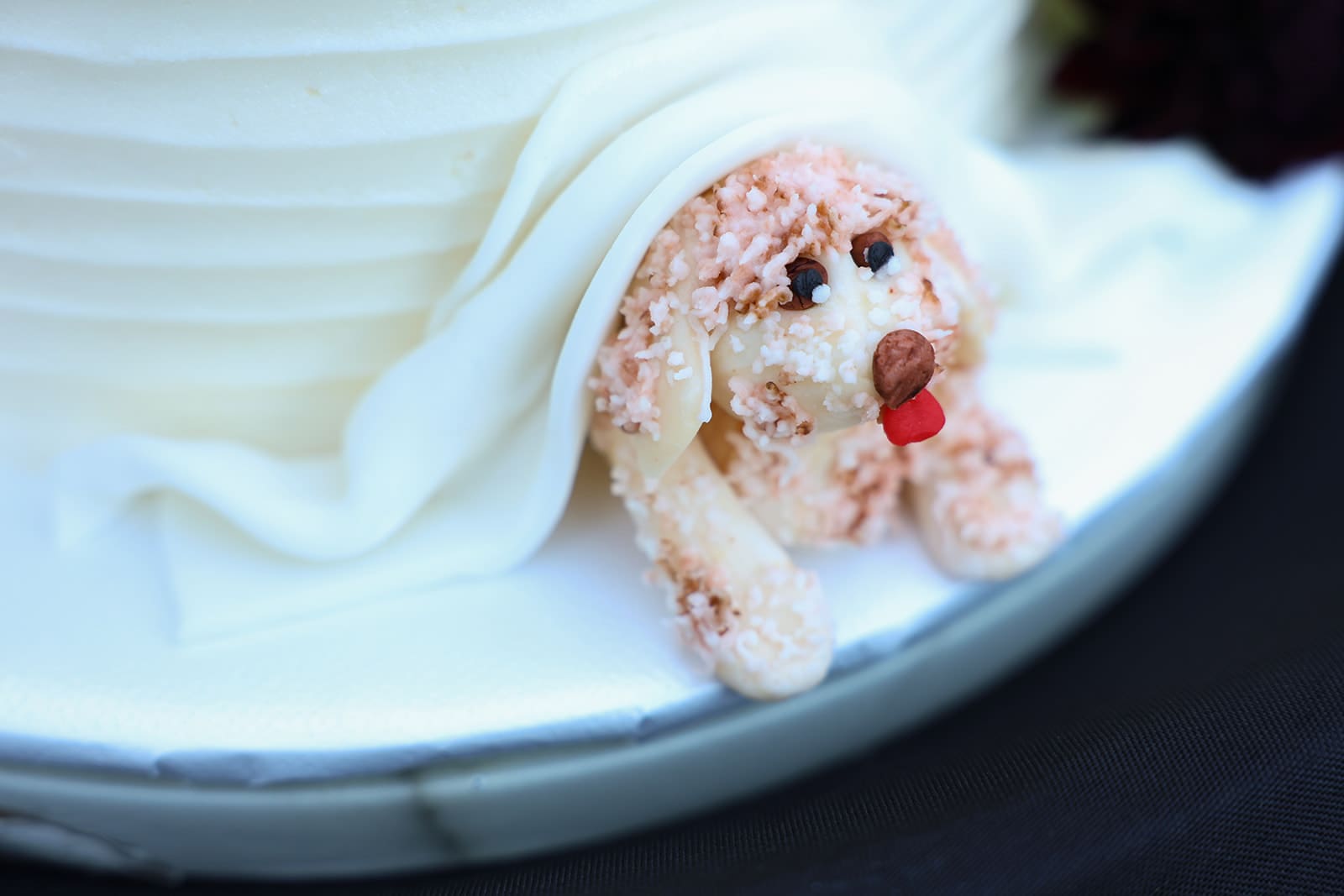 A playful detail from the wedding cake features a tiny edible dog sculpture peeking out from under fondant, adding a personal and whimsical touch.