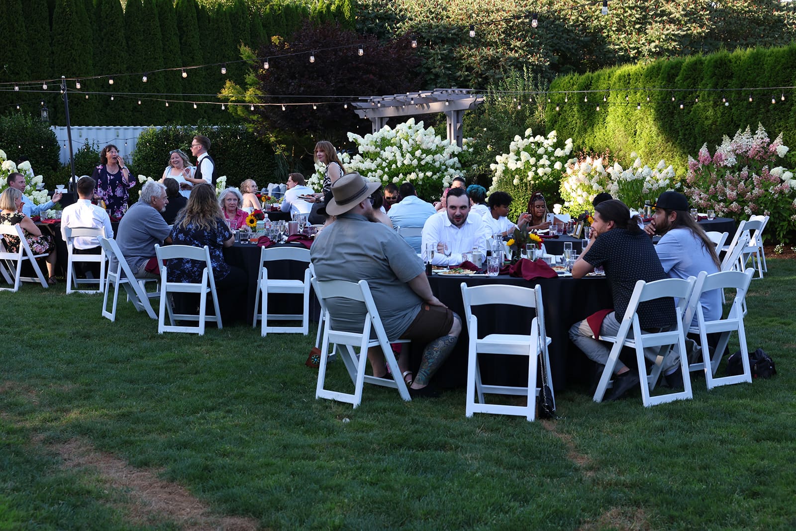 Guests enjoy a summer reception surrounded by blooming hydrangeas and string lights at an Oregon wedding venue.