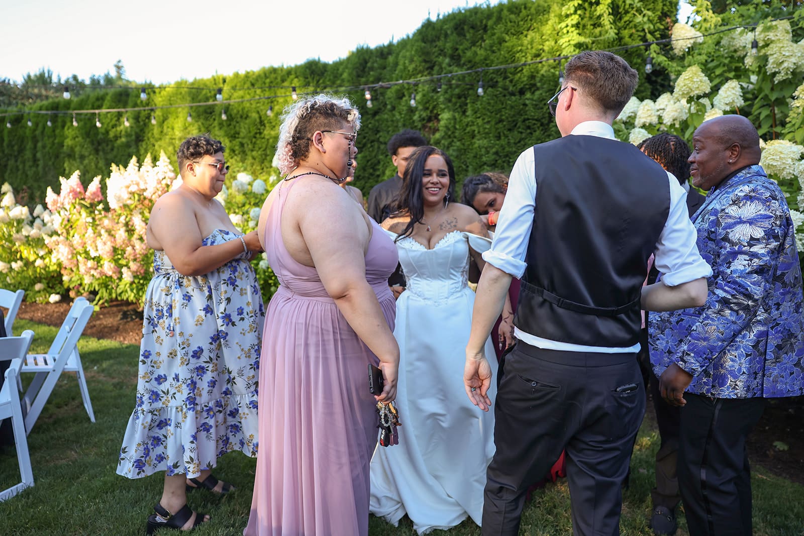 The bride and groom laugh and mingle with family and friends during golden hour, surrounded by string lights, florals, and a joyful energy at their Oregon wedding venue.