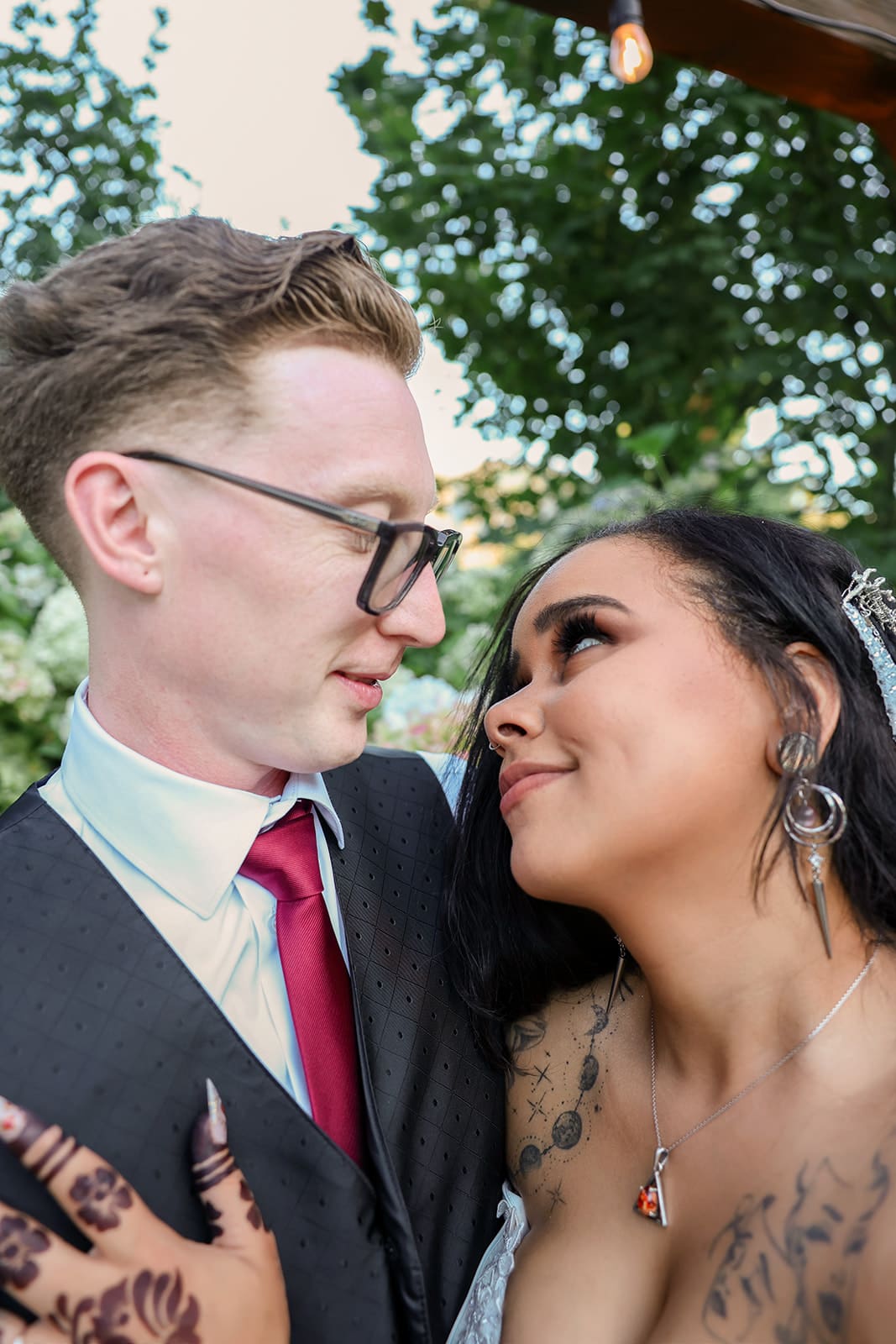 The bride and groom share an intimate, joy-filled moment beneath a canopy of trees at their Oregon wedding venue, both smiling with quiet tenderness.