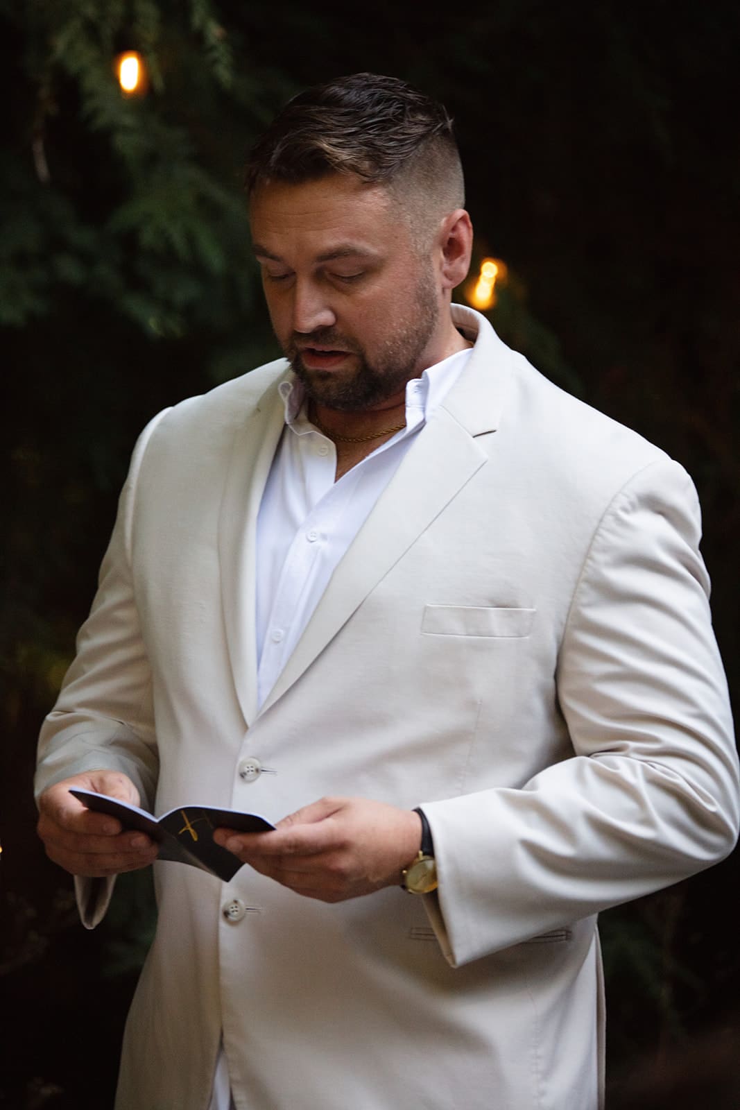 The groom stands in a light suit reading from a small vow book, surrounded by soft forest light — the kind of peaceful detail that makes airbnb weddings so special.