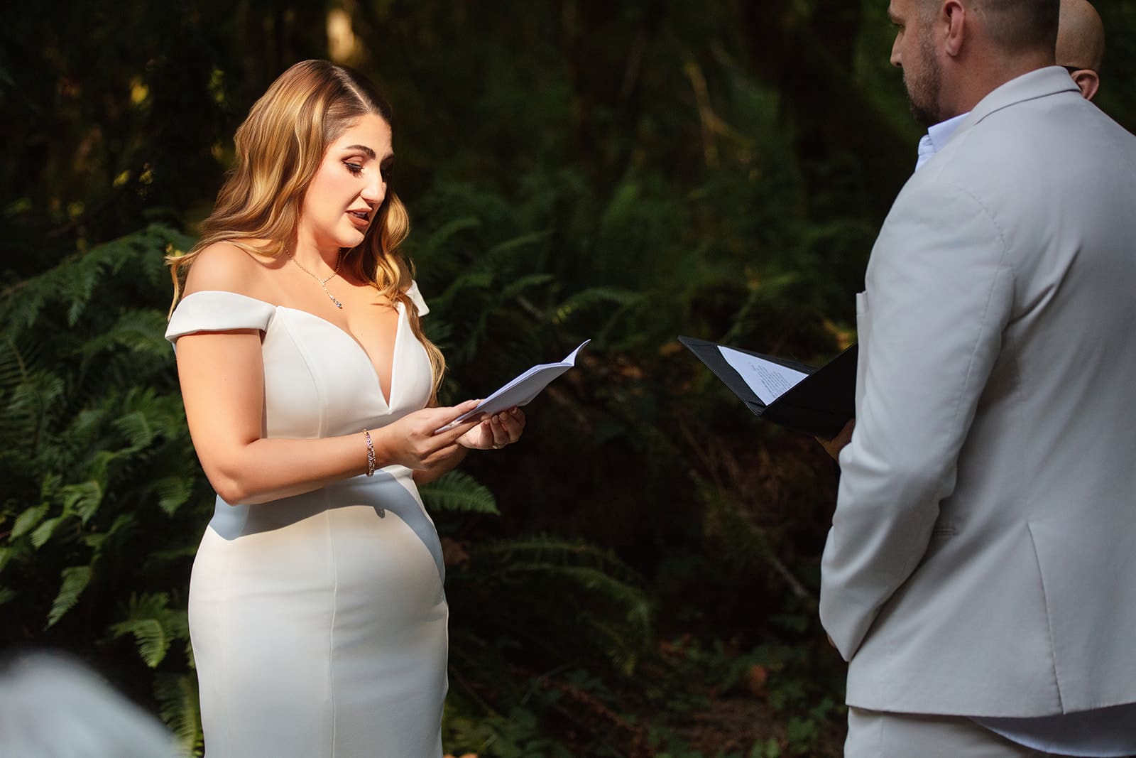 The bride reads heartfelt vows to her groom in the forest, emotion and sunlight framing the scene.