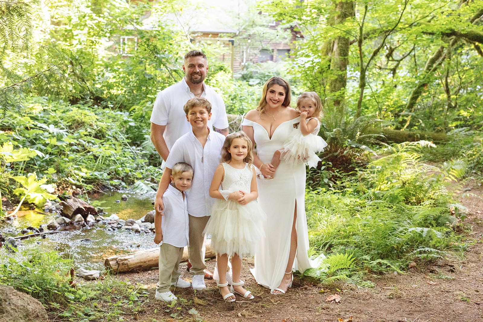 A family of six poses together by the creek, their outfits blending with the forest setting for a cozy, heartfelt airbnb weddings portrait.