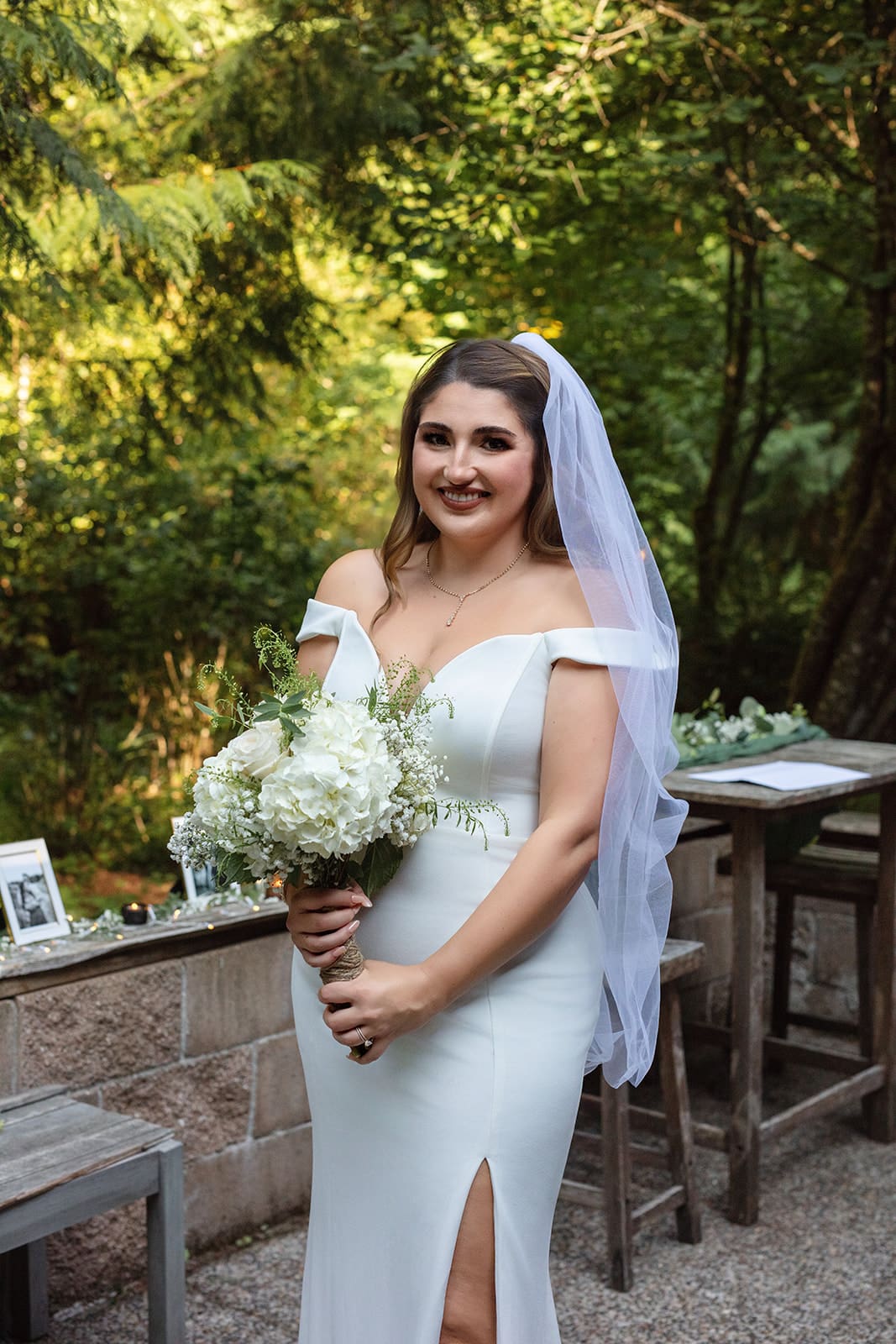 The bride poses with her bouquet and veil in the forest, her classic gown glowing in natural light.