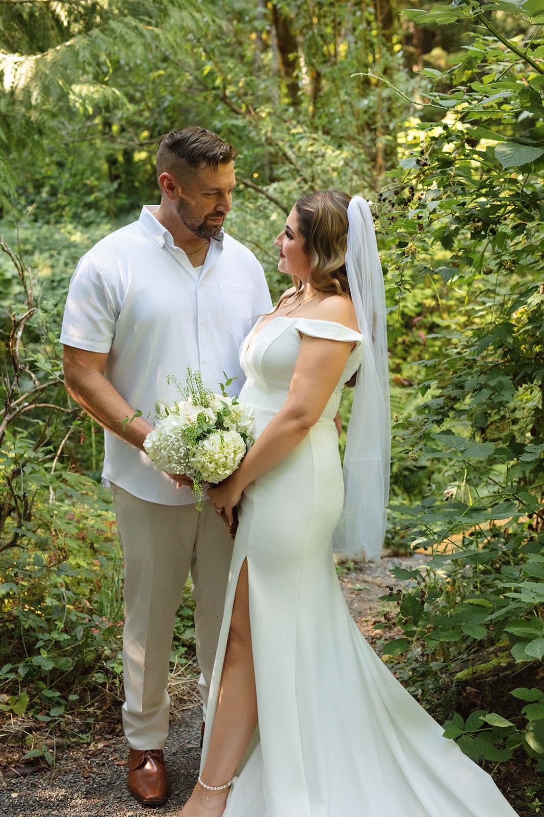 The couple shares a quiet moment surrounded by ferns and trees, her modern gown standing out against the greenery — a perfect example of airbnb weddings in nature.