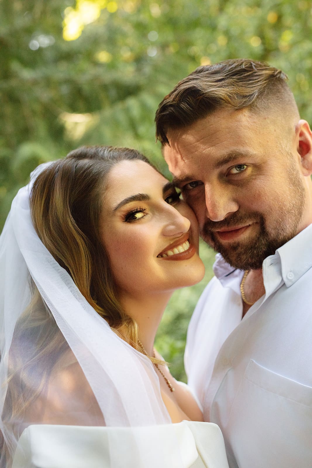 A portrait of the newlyweds surrounded by lush forest, the bride holding a bouquet of white flowers.