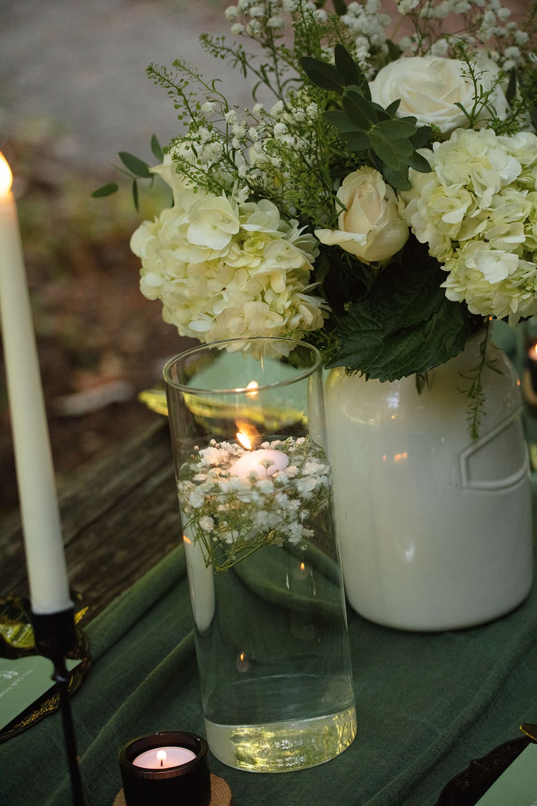 White hydrangeas and roses arranged beside floating candles on a green linen table runner — timeless decor for intimate airbnb weddings.