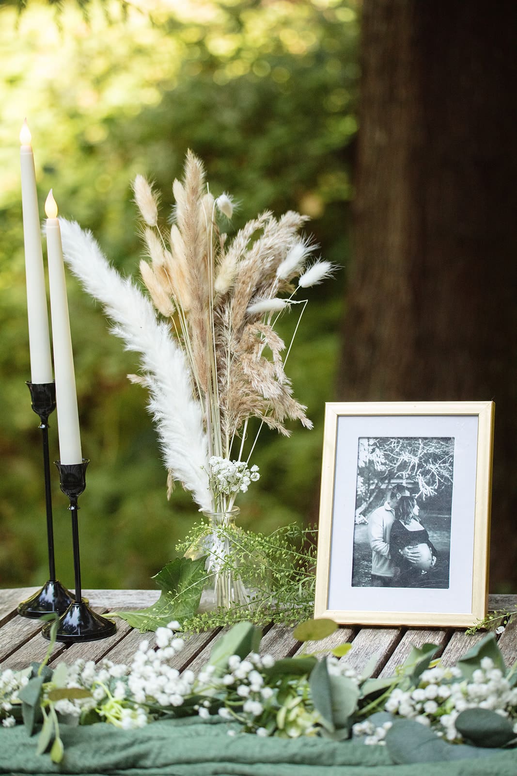 A sentimental wedding detail table with pampas grass, framed photo, and taper candles, styled with earthy textures.