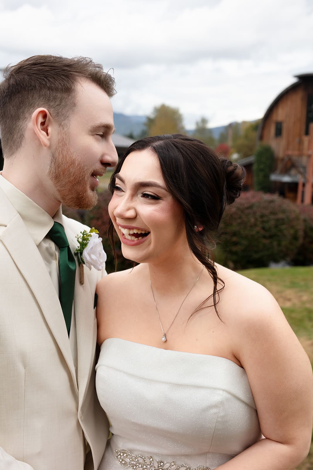 Joyful newlyweds sharing a laugh in front of a rustic barn venue on their wedding day.