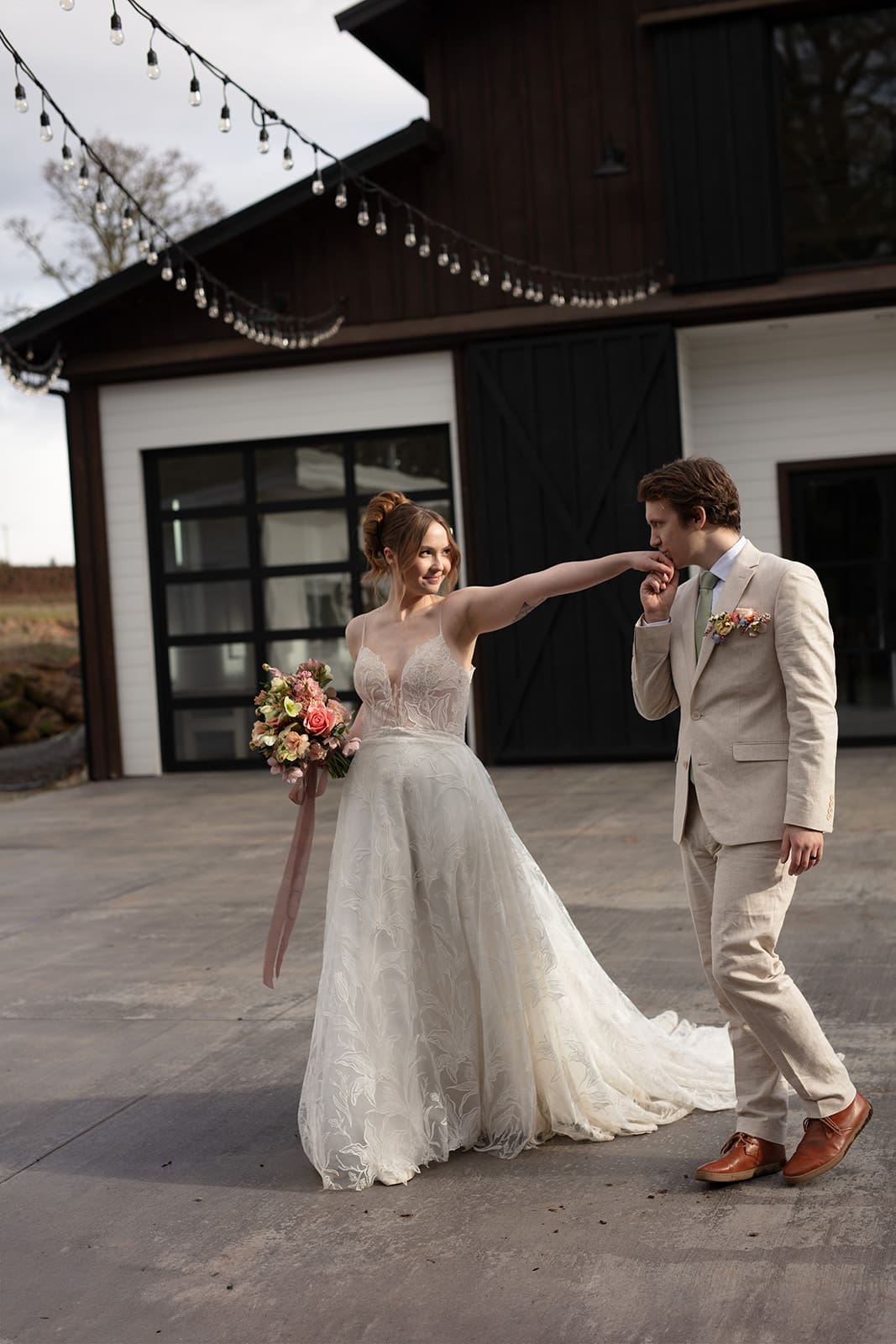 Elegant bride and groom sharing a sweet gesture outside a chic barn wedding venue.
