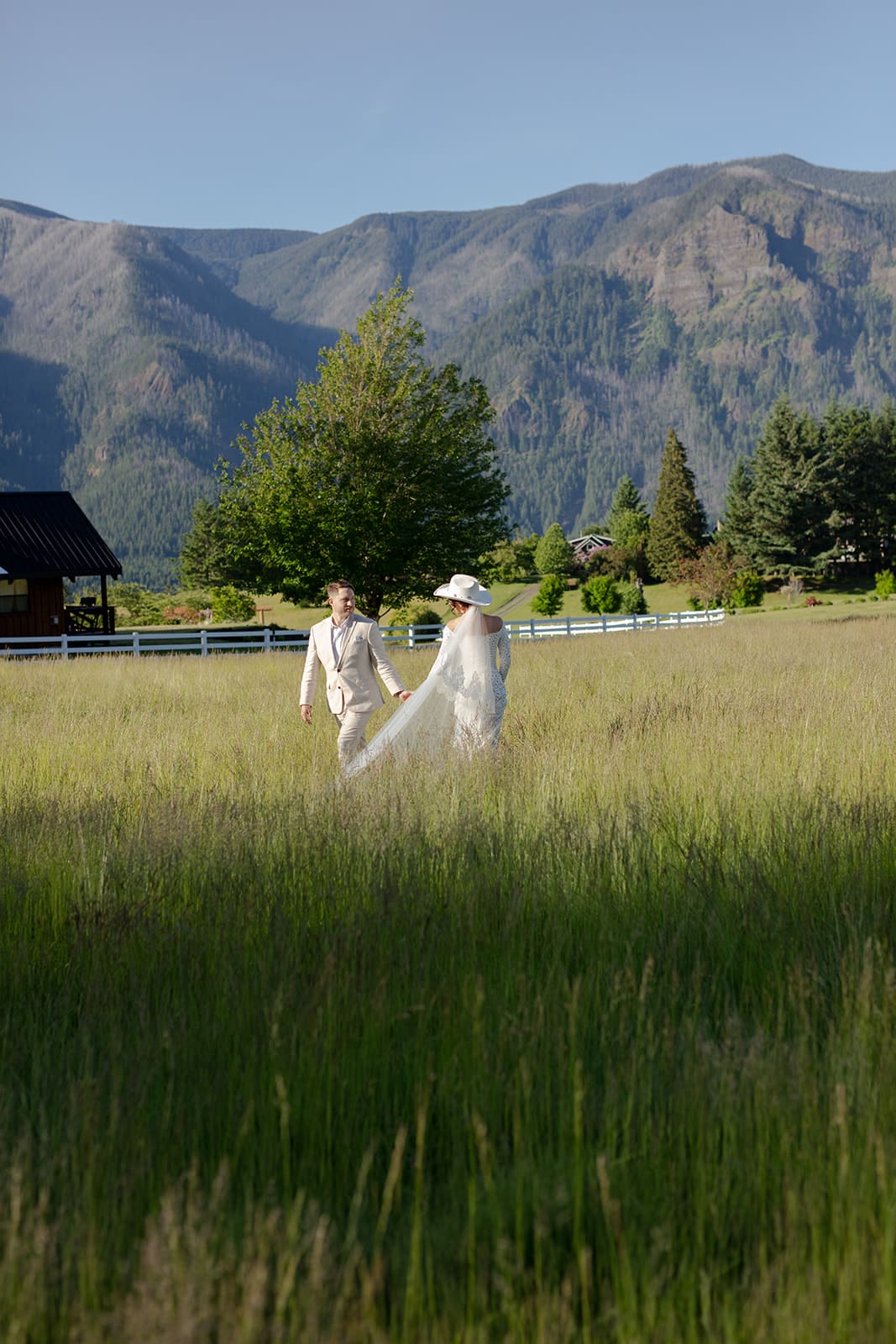 A scenic wedding in Washington state captured with a couple walking hand-in-hand through a meadow with mountain backdrops.