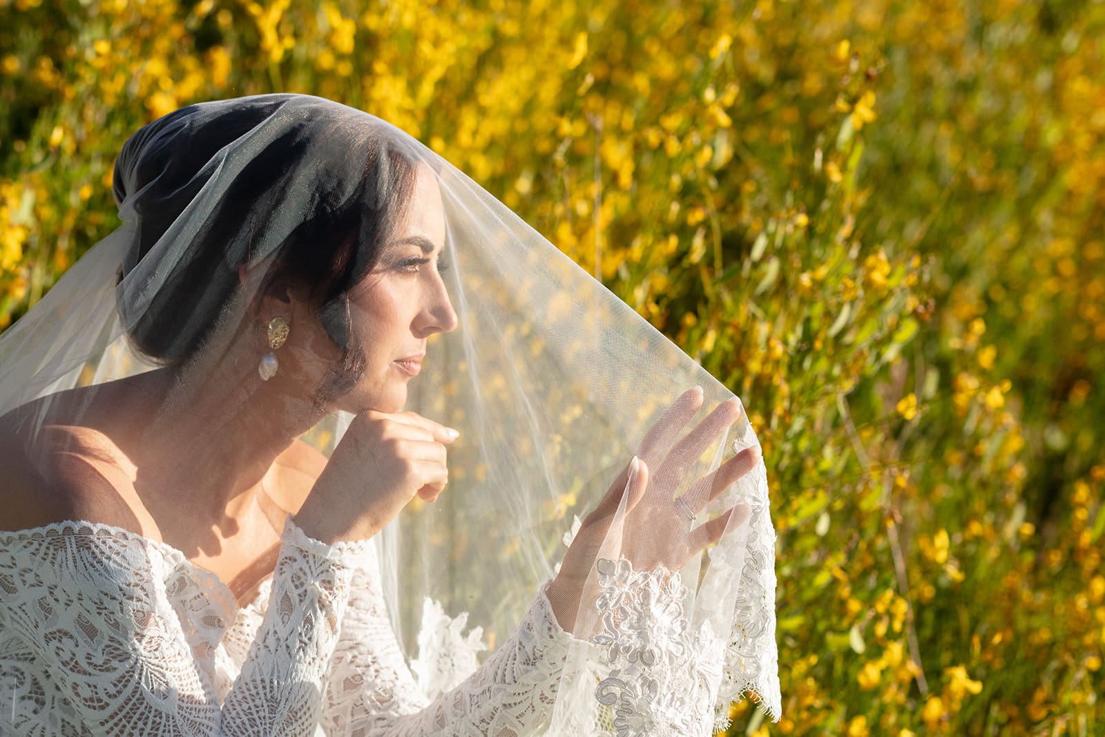Bride gazing thoughtfully under her veil, framed by vibrant wildflowers and golden evening light.